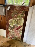 Full view of the rectangular onyx stone tabletop with a natural swirling pattern of green, red, and white colors, standing vertically.