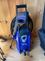 Front view of Blue Clean 527 pressure washer showing handle, hose wrapped on top, and front control panel with logo.