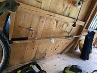 Roof snow rake pole and extension mounted on wooden wall with black snow scoop attachment visible nearby
