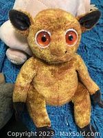 Golden-brown stuffed animal with large orange eyes, likely the kinkajou or similar toy.