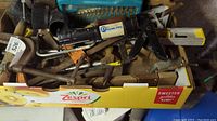 Photo showing a variety of hand tools including caulk dispensers, clamps, a level, and a box with drill bits.