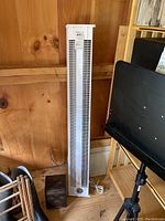 Photo of tall white Slant/Fin baseboard heater standing against wooden wall, electric cord visible.