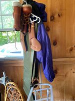 Photo showing the green waders hanging with Orvis fly fishing boots on hangers near a wooden wall and window.