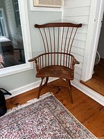 Vintage Windsor solid wood chair showing front view with spindle back and armrests on wooden floor with patterned rug nearby.