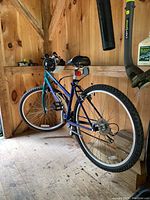 Photo of the blue Mongoose Switchback women's mountain bike with knobby tires in a wooden shed.