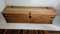 Closed pine wood chest trunk showing metal corner brackets and decorative metal latch on front.