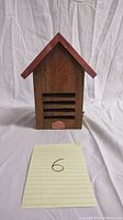 Front view of wooden bird feeder house showing ventilation slats and small opening at bottom.