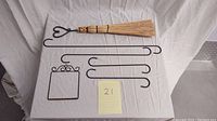 Top-down photo showing decorative straw broom and five black metal hooks arranged on white cloth with a note showing '21'