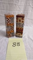 Two handmade rectangular decorative candles with hand-painted patterns standing upright, showing their designs.