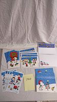 Photo showing multiple Peanuts Christmas cards including Snoopy and Charlie Brown characters, displayed on fabric background with matching white envelopes with decorative blue Peanuts flap.
