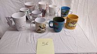 Photo showing all 11 mugs arranged in two rows, displaying various shapes and different graphics including The Lorax and Vancouver Olympics.
