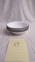 Stack of 6 white Corelle soup bowls with black stripe around rim, shown from side angle.