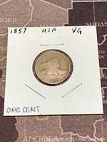 Obverse side of the 1857 flying eagle penny, showing the eagle in flight and year 1857 at bottom, mounted in a white 2x2 holder marked with year, USA and VG condition.