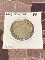Obverse side of the 1869 Jamaica Queen Victoria One Penny coin in holder showing Queen Victoria seated image.
