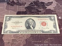 Front side of the 1953 US $2 banknote laid flat on a world map background, showing serial number and denomination.