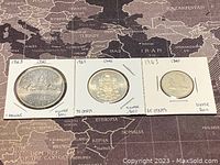 Three 1963 Canadian silver coins mounted in holders showing reverse sides: dollar with canoe, 50 cents with coat of arms, 25 cents with caribou.