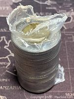 Stacked roll of 1996 Canadian twoonie coins showing the top coin and partial wrapping seen from the side with torn plastic ends.