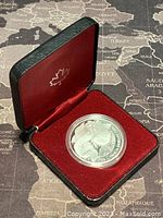 Coin displayed in its black presentation case with red velvet and satin interior featuring a maple leaf emblem on the lid.