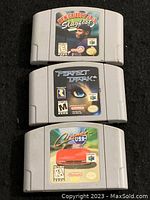 Three Nintendo 64 game cartridges stacked: Ken Griffey Jr.'s Slugfest on top, Perfect Dark in middle, and Cruis'n USA on bottom. Each cartridge label is visible showing artwork and title.
