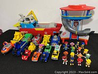 Wide shot of Paw Patrol toys collection showing vehicles, figures, and playset on black surface