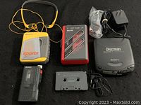 Lot items displayed on black backdrop including all players, headphones, charger, earphones, and cassette tape.
