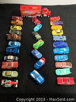 Full set of 30 Cars die cast toy vehicles arranged showing all characters in varying colors with Mack semi-truck and trailer on black background.