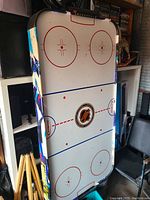 Full view of the air hockey table standing upright, showing the NHL-style hockey rink graphics on the playing surface and colorful side panels.