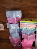 Stacked bath bombs in pink and blue star shapes with accompanying box on wooden surface.