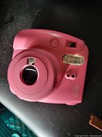Pink Fujifilm Instax Mini 11 instant camera showing front details: lens, flash, viewfinder.