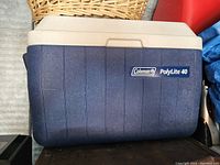 Photo showing the front and side profile of a Coleman PolyLite 40 cooler with blue textured plastic body and beige lid.