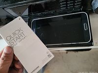 Photo of Quick Start Guide booklet held over Samsung smartphone with screen off.