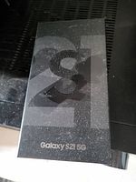Original black retail box of the Samsung Galaxy S21 5G smartphone with visible wear and dust.