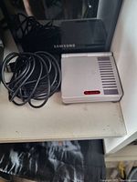 Closed Nintendo Gameboy Advance SP with attached power cable and charging adapter alongside a Samsung device.