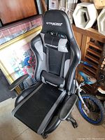 Photo of a black and gray GTRacing gaming chair with lumbar and neck support cushions, adjustable armrests, and caster wheels.