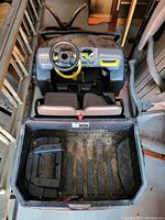 Top-down view of a black and yellow electric ride-on kids car with two seats, a steering wheel, dashboard controls, and rear cargo area showing dirt and wear.