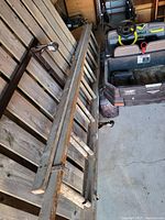 Large wooden ladder consisting of two sections, laid horizontally on wooden planks with part of a riding lawn mower visible nearby.