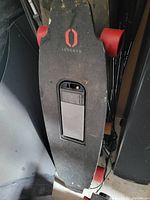 Photo of black Onewheel motorized skateboard with visible battery compartment and red wheels.