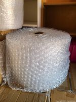 Large roll of clear bubble wrap placed on a cardboard box with a hole in the center for holding the roll, showing texture and size.