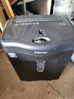 Black Fellowes paper shredder with top feed slot, control knob, and waste bin with transparent window.