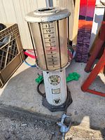 Full view of the vintage gasoline pump showing the cylindrical glass tank with measurement markings and metal base with a nozzle attached.