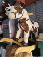 Plush rocking horse with brown and white patches on a wooden rocking base with decorative carving.