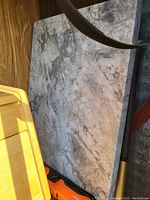 Rectangular stone cutting board with marbled gray pattern on a wooden floor next to other objects
