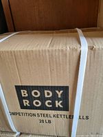 Photo of plain cardboard box for Body Rock 20 lb competition steel kettlebells secured with two white straps.