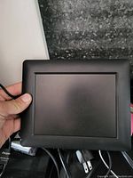 Front view of the black USB picture frame showing the LCD screen and attached USB cable held in hand.