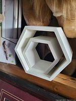Two white hexagonal wall shelves nested, showing shape and size difference.