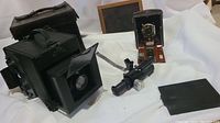 Front and side view of vintage pocket Poco camera with wood and leather body, telescopic attachment, and Auto Graflex camera case with leather strap.