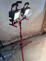 Twin-head Craftsman worklight with two swivel lights mounted on a red tripod stand placed in a concrete basement setting.