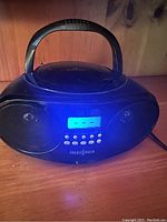 Front view of Insignia black portable CD boombox showing speakers, control buttons, LED display and carrying handle.