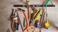 Photo showing an assortment of large tools including saws, crowbar, rubber mallet, extension cords, and hand tools spread on a concrete floor.