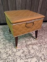 Photo of the gold quilted vinyl storage bench showing its side profile with brass handle and tapered wood legs capped with brass.